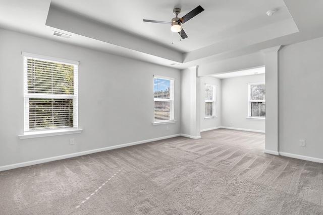 carpeted spare room featuring a healthy amount of sunlight, a tray ceiling, and ceiling fan