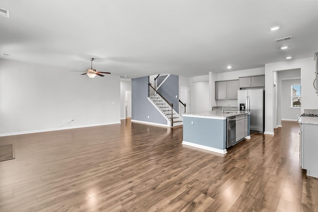 kitchen featuring gray cabinetry, stainless steel appliances, dark wood-type flooring, and a center island with sink