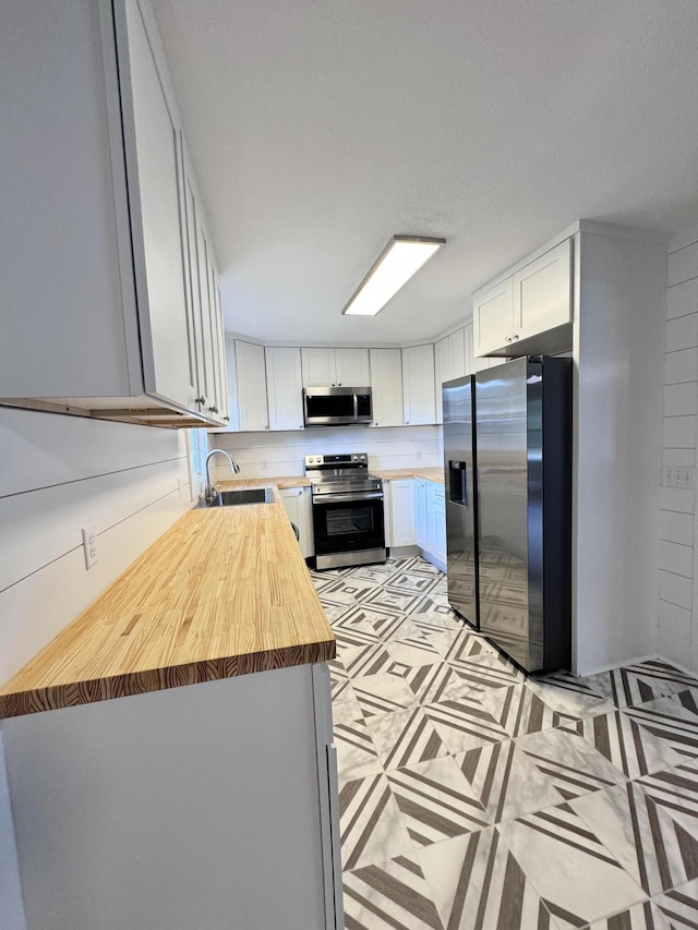 kitchen featuring stainless steel appliances, white cabinetry, sink, and wooden counters