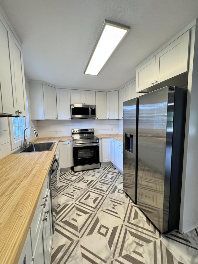 kitchen with wooden counters, appliances with stainless steel finishes, and white cabinets