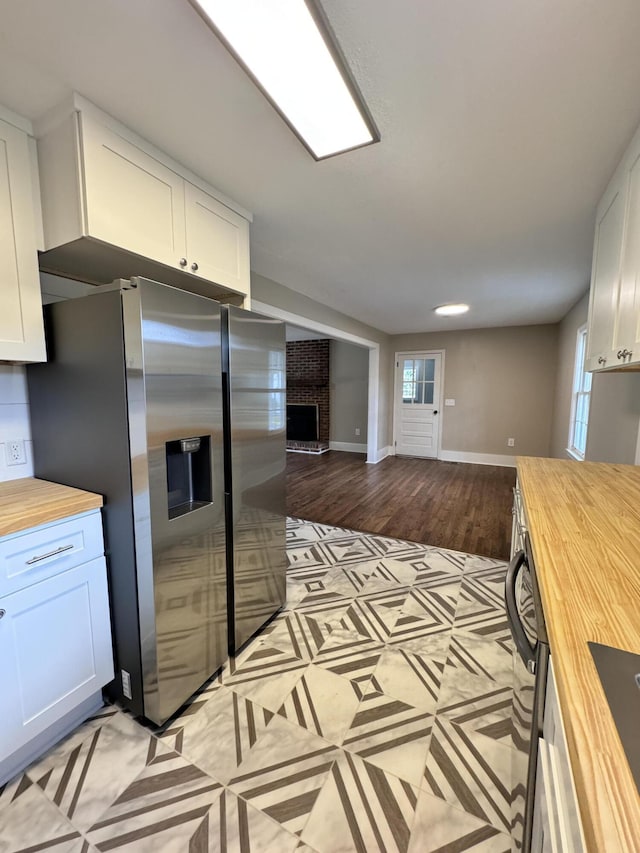 kitchen with white cabinetry, butcher block counters, stainless steel refrigerator with ice dispenser, a brick fireplace, and light wood-type flooring