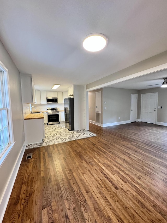 unfurnished living room with ceiling fan, sink, and light hardwood / wood-style flooring