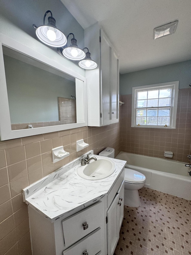 full bathroom featuring tiled shower / bath combo, vanity, tile walls, and toilet