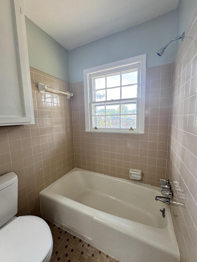 bathroom featuring toilet, tiled shower / bath combo, tile patterned flooring, and tile walls