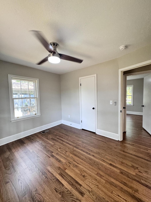 unfurnished room featuring dark hardwood / wood-style flooring, ceiling fan, a textured ceiling, and a healthy amount of sunlight