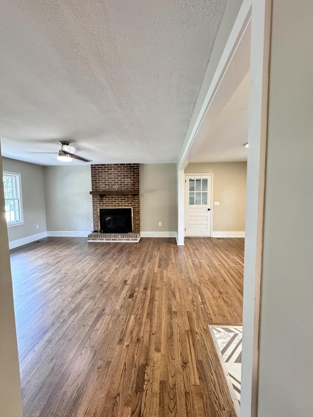 unfurnished living room featuring hardwood / wood-style flooring, ceiling fan, a fireplace, and a textured ceiling