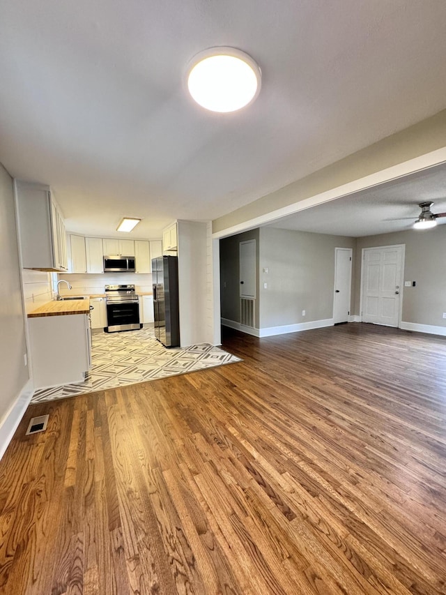 unfurnished living room with sink, ceiling fan, and light wood-type flooring