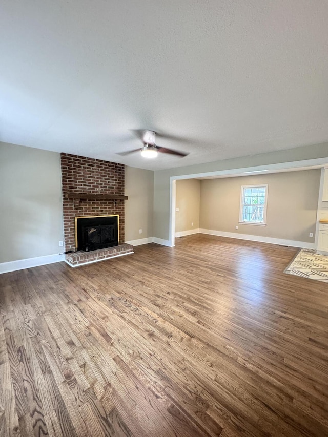 unfurnished living room with ceiling fan, a fireplace, hardwood / wood-style floors, and a textured ceiling