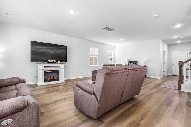 living room with visible vents, light wood-style floors, a warm lit fireplace, and stairs