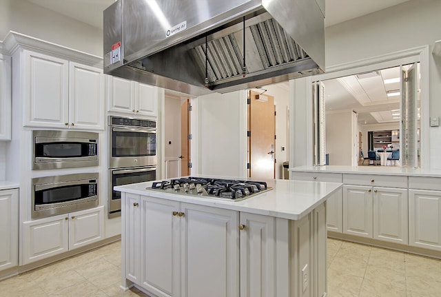 kitchen featuring light tile patterned flooring, white cabinetry, a center island, stainless steel appliances, and wall chimney range hood