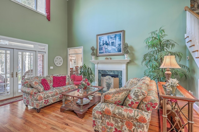 living room featuring a premium fireplace, french doors, light hardwood / wood-style floors, and a high ceiling