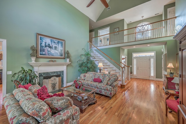 living room featuring ceiling fan, a fireplace, wood-type flooring, and a high ceiling