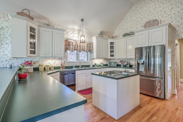 kitchen featuring white cabinetry, hanging light fixtures, stainless steel appliances, light hardwood / wood-style flooring, and vaulted ceiling