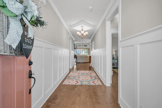 hall with ornamental molding, a notable chandelier, and light wood-type flooring