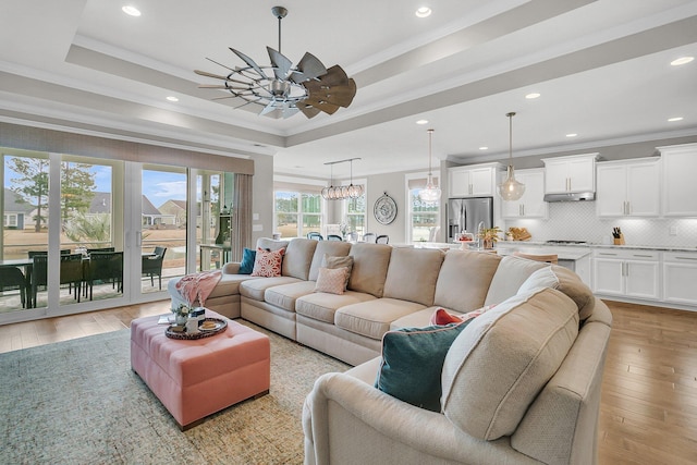 living room featuring a tray ceiling, ornamental molding, ceiling fan, and light wood-type flooring