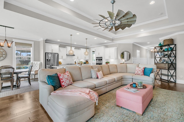 living room with crown molding, dark wood-type flooring, ceiling fan with notable chandelier, and a tray ceiling