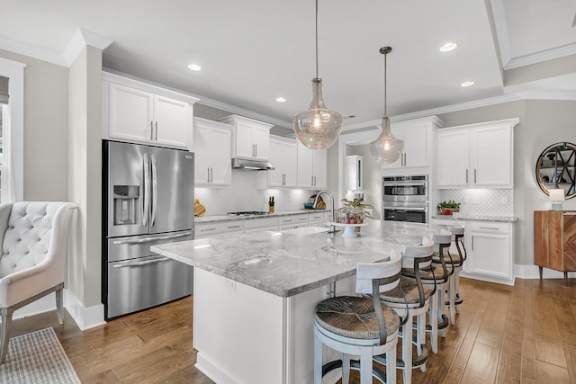 kitchen featuring sink, white cabinetry, a kitchen island with sink, stainless steel appliances, and decorative light fixtures