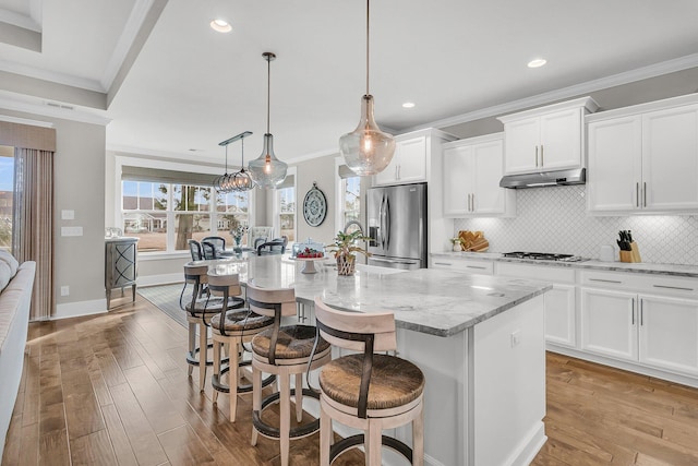 kitchen featuring a kitchen island with sink, stainless steel appliances, light stone countertops, white cabinets, and decorative light fixtures