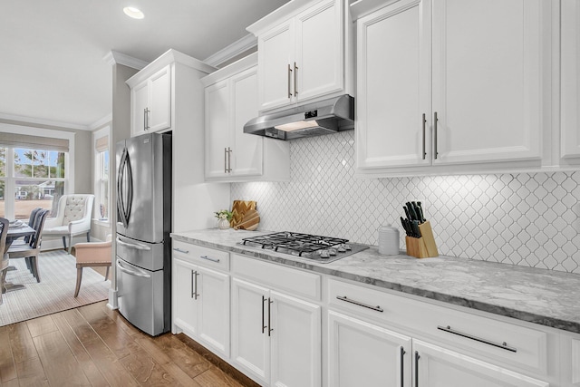 kitchen with white cabinetry, crown molding, appliances with stainless steel finishes, light stone countertops, and hardwood / wood-style floors