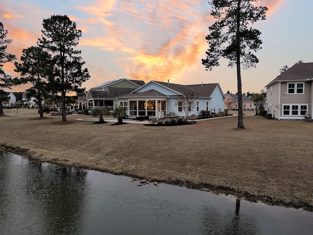 back house at dusk with a water view and a lawn