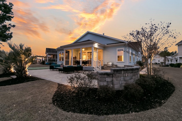 back house at dusk featuring an outdoor living space, a patio, and a sunroom