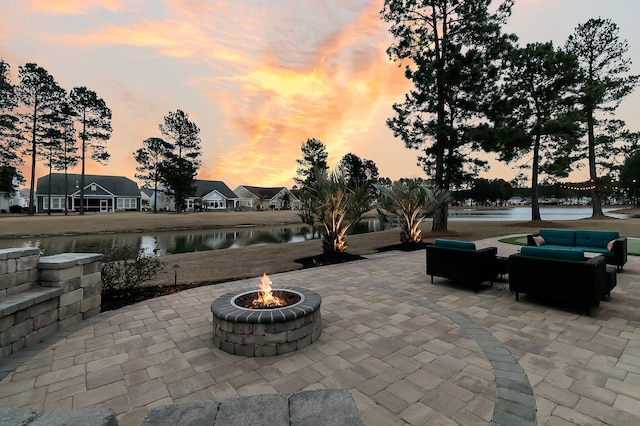 patio terrace at dusk featuring a water view and an outdoor living space with a fire pit