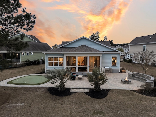 back house at dusk featuring a patio area, a fire pit, and a lawn