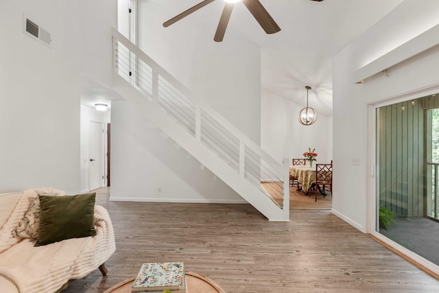 living area featuring stairs, wood finished floors, a ceiling fan, a towering ceiling, and baseboards