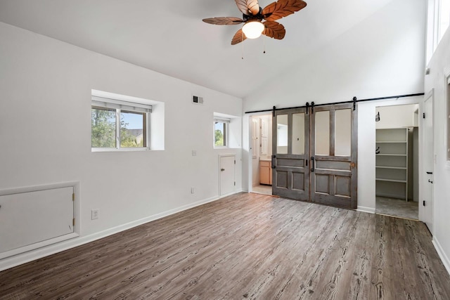 unfurnished bedroom featuring a barn door, high vaulted ceiling, wood finished floors, baseboards, and connected bathroom