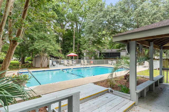 community pool featuring a deck, a storage unit, a fenced backyard, an outbuilding, and a patio area