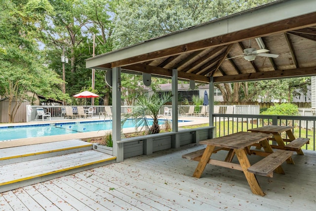 deck with a ceiling fan, a fenced backyard, a community pool, a gazebo, and a storage shed