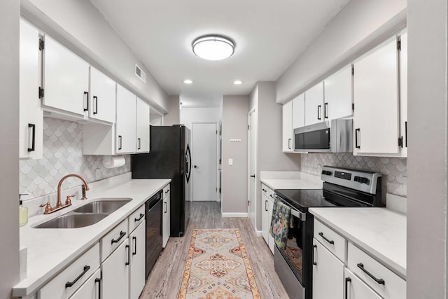 kitchen featuring black appliances, a sink, light wood-style flooring, white cabinets, and decorative backsplash