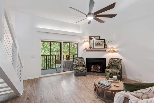 living area with a fireplace, wood finished floors, ceiling fan, and baseboards