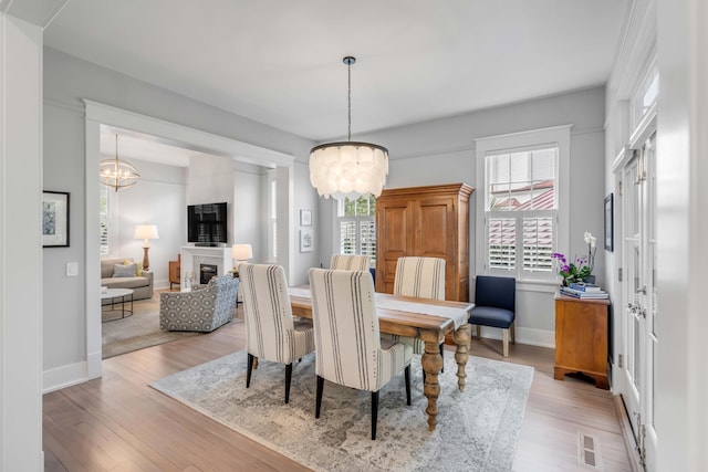 dining area featuring a glass covered fireplace, visible vents, baseboards, and light wood-style floors