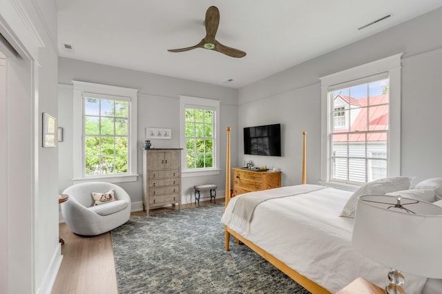 bedroom with a ceiling fan, wood finished floors, visible vents, and baseboards