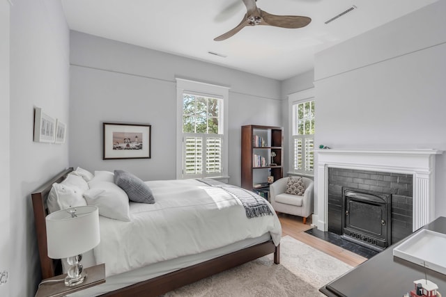 bedroom featuring a fireplace with flush hearth, wood finished floors, visible vents, and ceiling fan