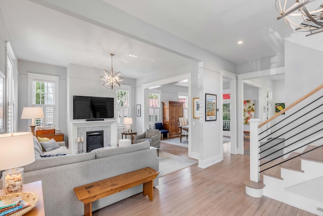 living room with a chandelier, stairs, a premium fireplace, recessed lighting, and light wood-style flooring