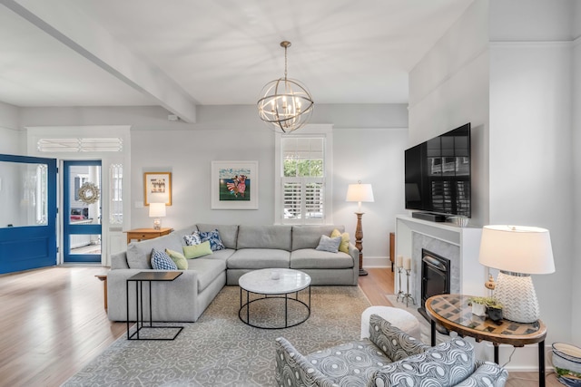 living room featuring beam ceiling, a notable chandelier, wood finished floors, a high end fireplace, and baseboards