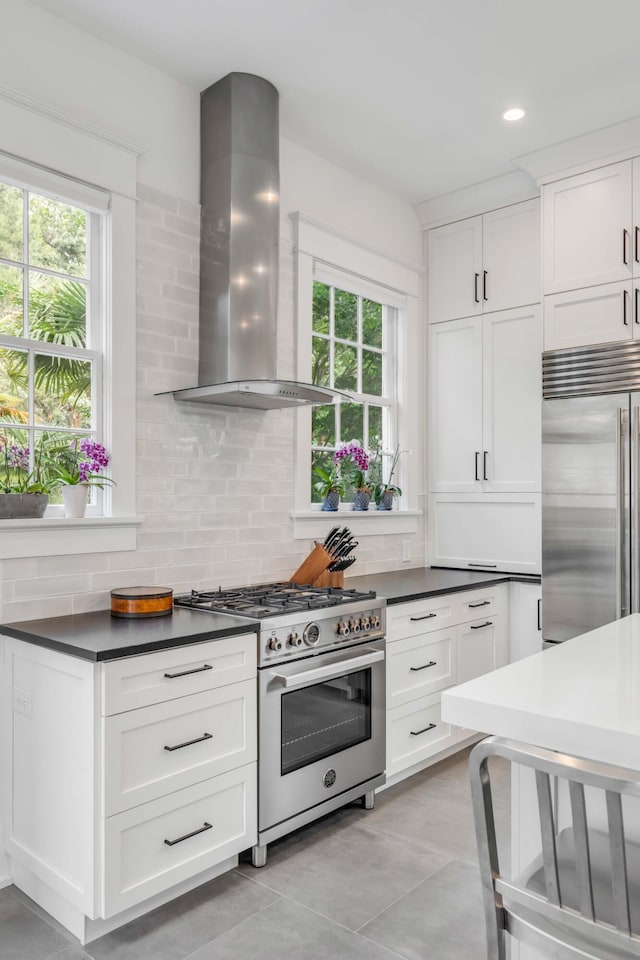 kitchen with a wealth of natural light, backsplash, high end appliances, and wall chimney range hood