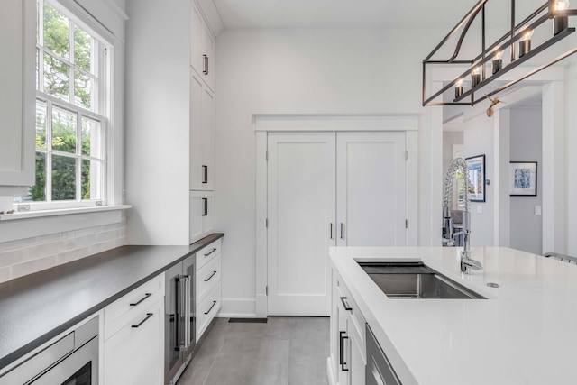 kitchen with pendant lighting, beverage cooler, a sink, stainless steel microwave, and white cabinetry