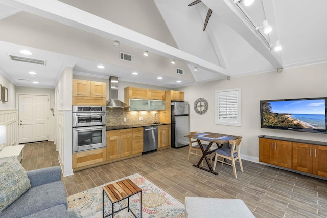 kitchen featuring sink, wall chimney exhaust hood, vaulted ceiling with beams, appliances with stainless steel finishes, and light wood-type flooring