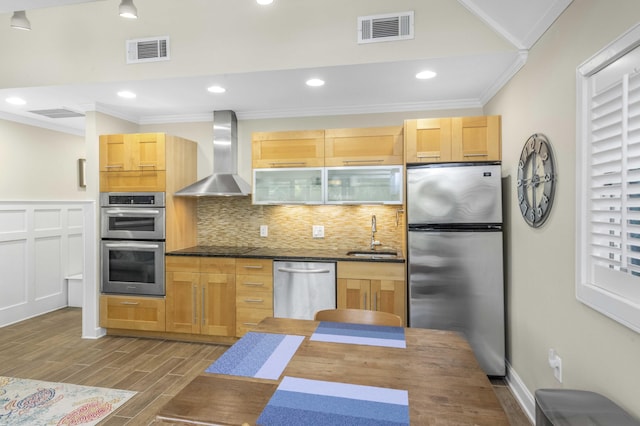 kitchen with appliances with stainless steel finishes, backsplash, ornamental molding, wall chimney exhaust hood, and light brown cabinets