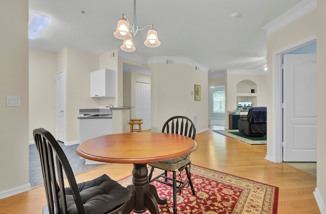 dining area with ornamental molding, light hardwood / wood-style flooring, a notable chandelier, and built in shelves