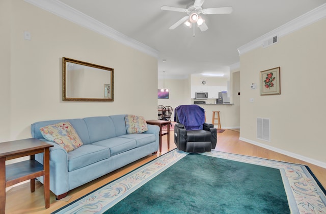 living room featuring ceiling fan with notable chandelier, wood-type flooring, and crown molding