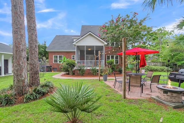 rear view of house with a sunroom, a yard, a patio area, and a fire pit