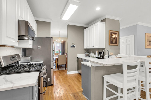 kitchen featuring a breakfast bar, pendant lighting, white cabinets, ornamental molding, and stainless steel appliances