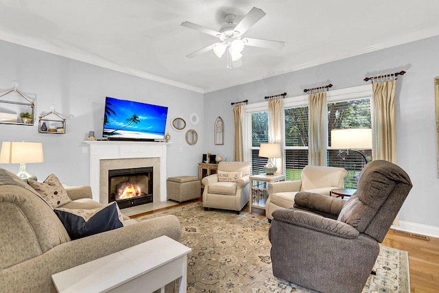 living room with ceiling fan, crown molding, a fireplace, and light hardwood / wood-style floors