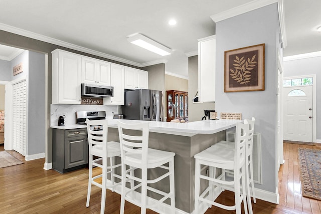 kitchen featuring crown molding, a breakfast bar, hardwood / wood-style floors, stainless steel appliances, and white cabinets