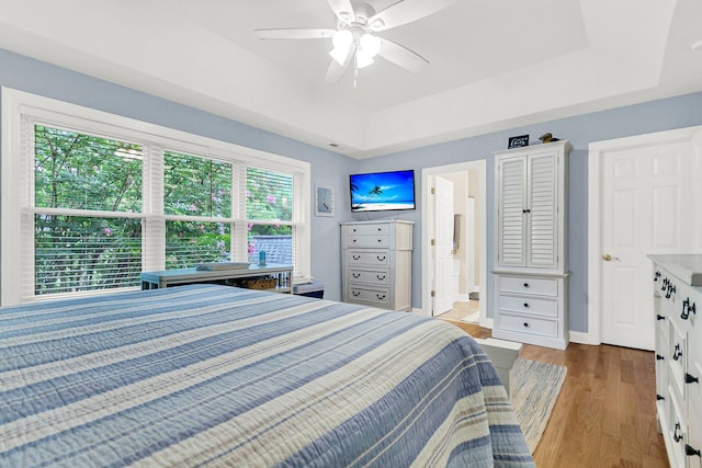 bedroom with connected bathroom, light hardwood / wood-style flooring, a raised ceiling, and ceiling fan