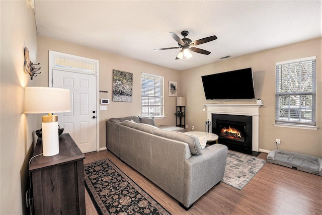 living area with a fireplace with flush hearth, visible vents, a ceiling fan, and wood finished floors